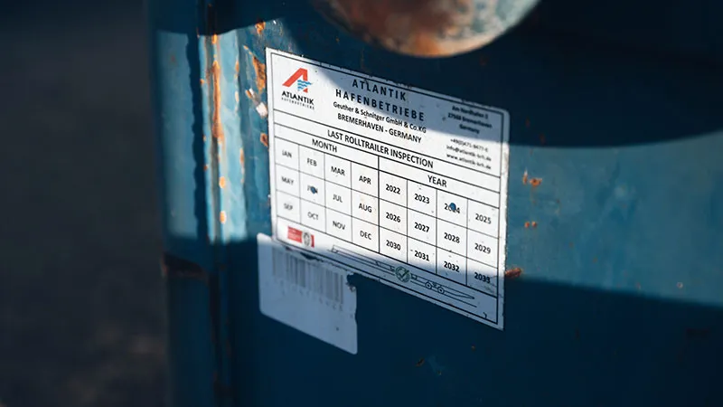 Close-up of an inspection sticker on a blue metal surface, indicating months and years for recording occupational safety inspections, with handwritten markings in several boxes.