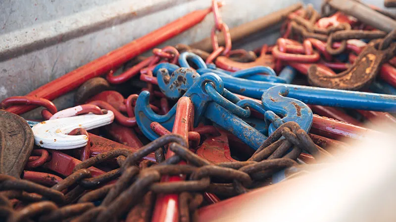 A close-up of a pile of metal chains and colorful hooks, including blue, red, and white parts, tangled in a metal container.